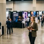 Every Event You Attend Is an Intelligence Operation - Are You Running One? Woman with notebook checking out booth competition